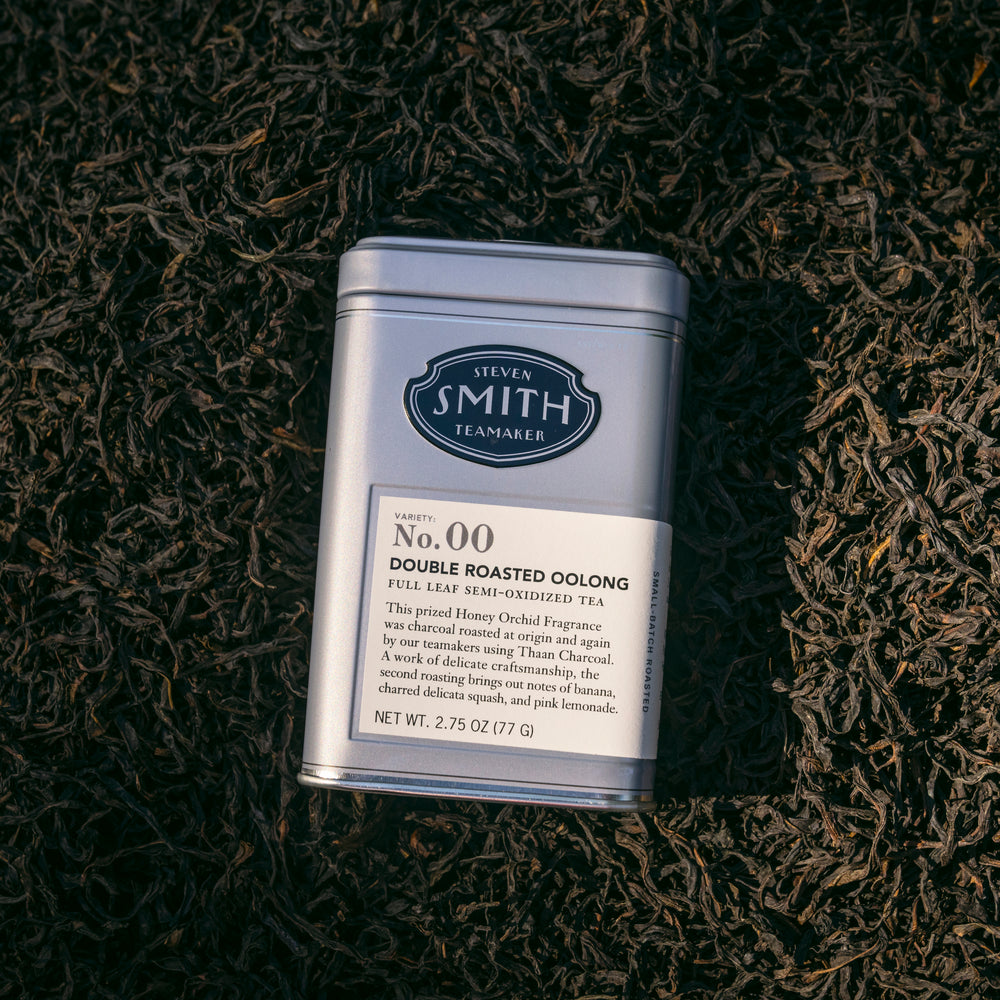 Grey tin of Double Roasted Oolong tea laying on a bed of loose leaf oolong tea.