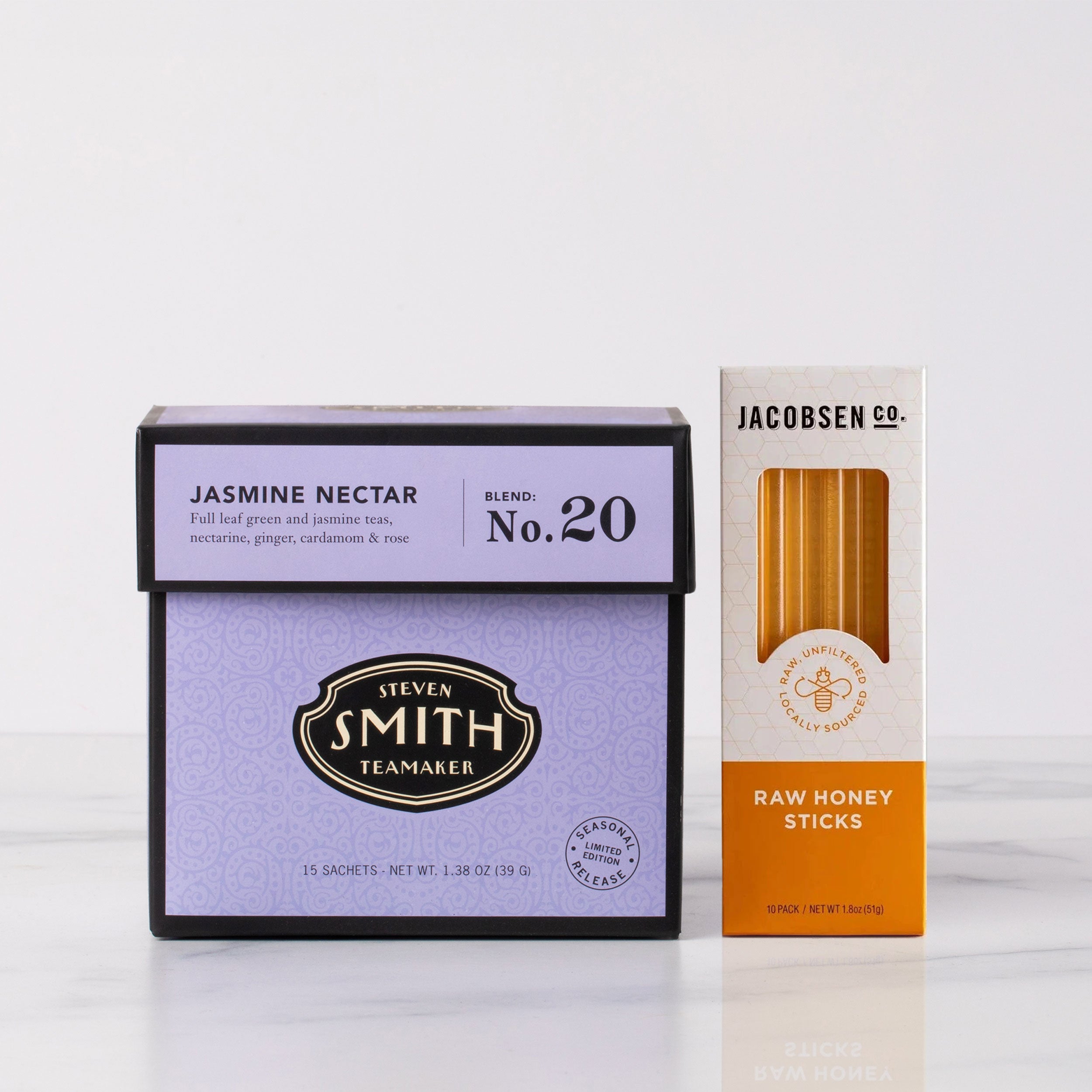 Two product boxes, one for Steven Smith Jasmine Nectar tea and the other for Jacobsen's Raw Honey Sticks, on a white background.