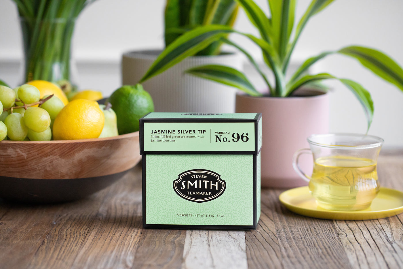 Box of Jasmine Silver Tip green tea on a table next to a clear tea cup filled with green tea.