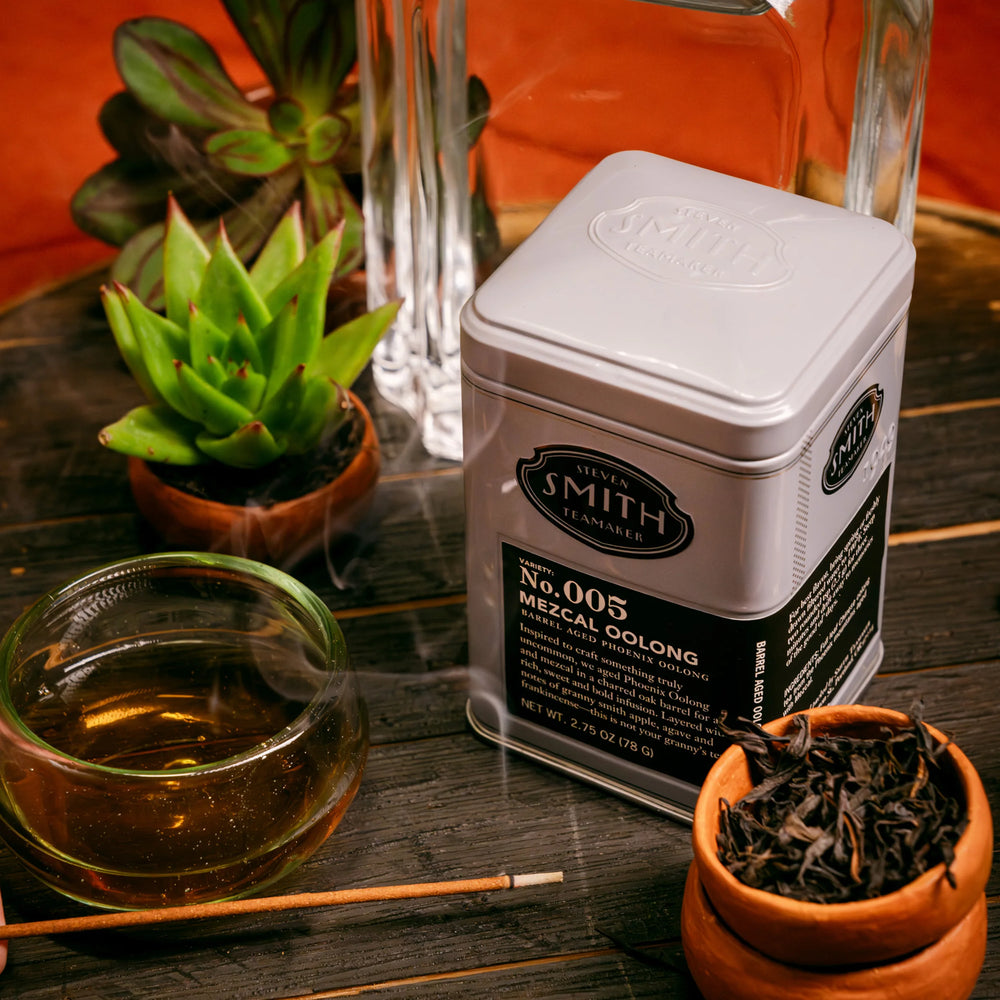 Mezcal Oolong tea canister labeled 'Smith' with a glass of tea and potted plants on a wooden surface