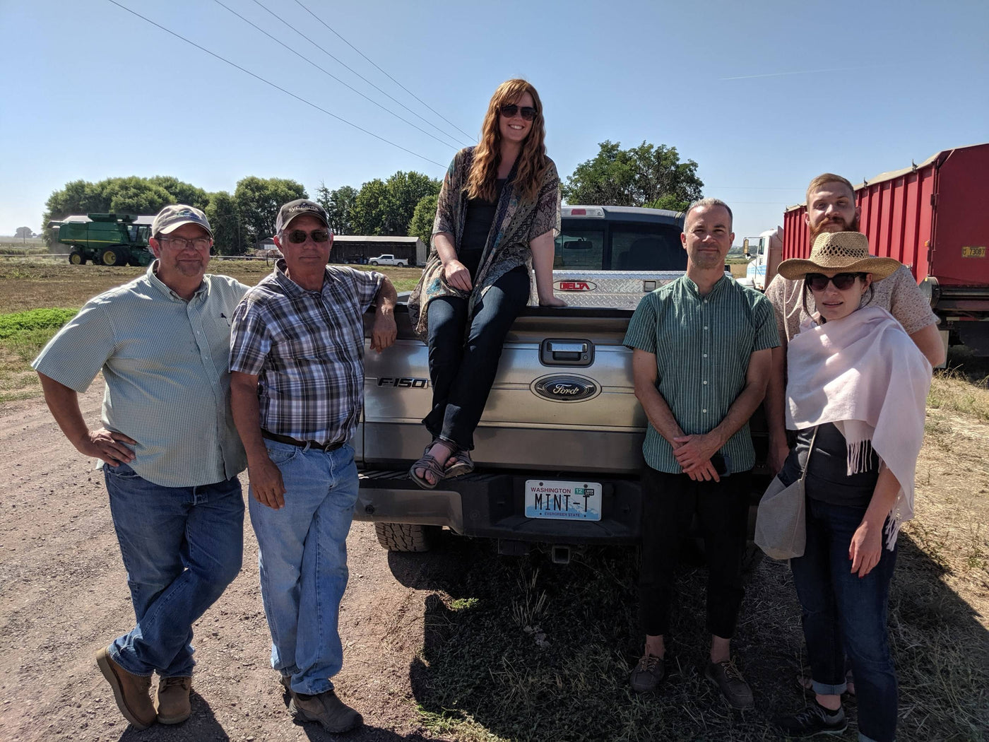 Teamakers and peppermint farmers stand proudly in front of a pick-up truck with a license plate that reads "Mint-T".