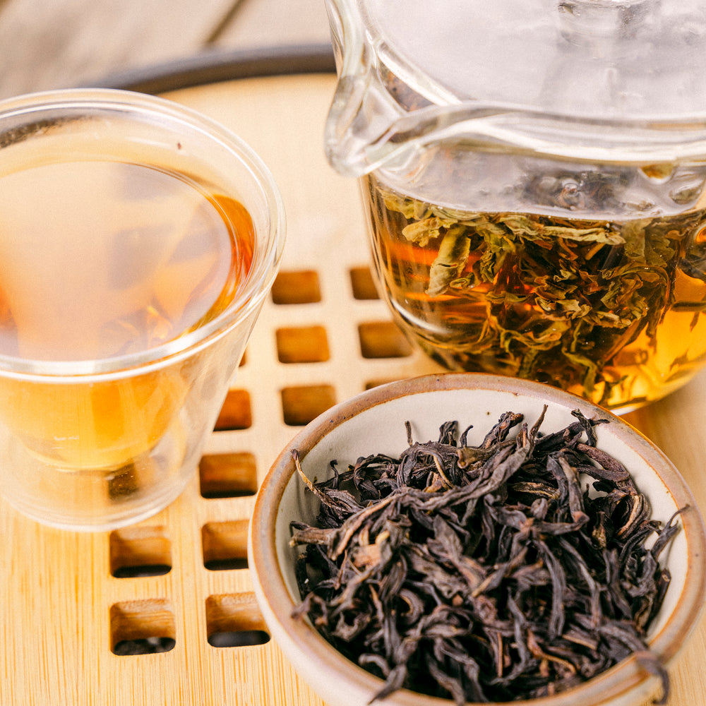 Close up of brewing Phoenix Oolong to produce a golden tea next to a dish filled with loose Phoenix Oolong tea.