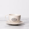 Porcelain teacup and saucer with black Smith logo shield on the front of teacup..