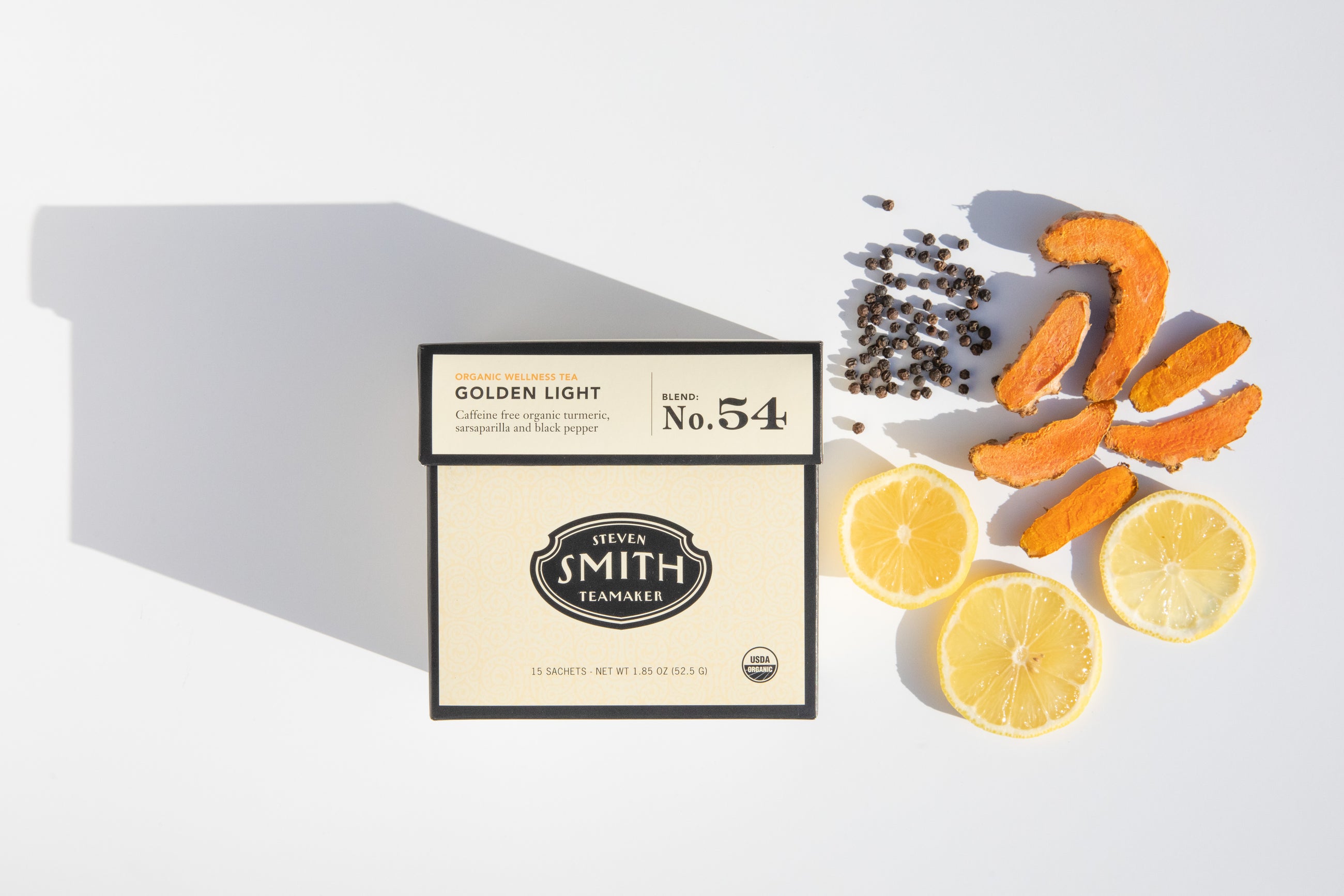 Box of Golden Light on white background with pile of black pepper, sliced turmeric root and lemon slices.