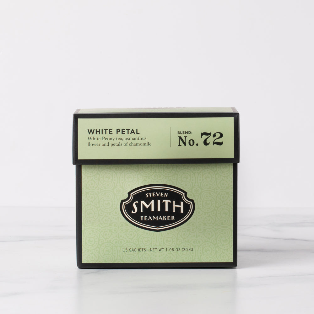 Green box of white petal tea on marble table.