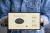 Person holding cream box with black trim.