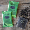Two green metallic sachets of tea on wooden background.