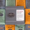Grey box with embossed Smith logo shield and white label on top of green, black and orange sachets around the box.