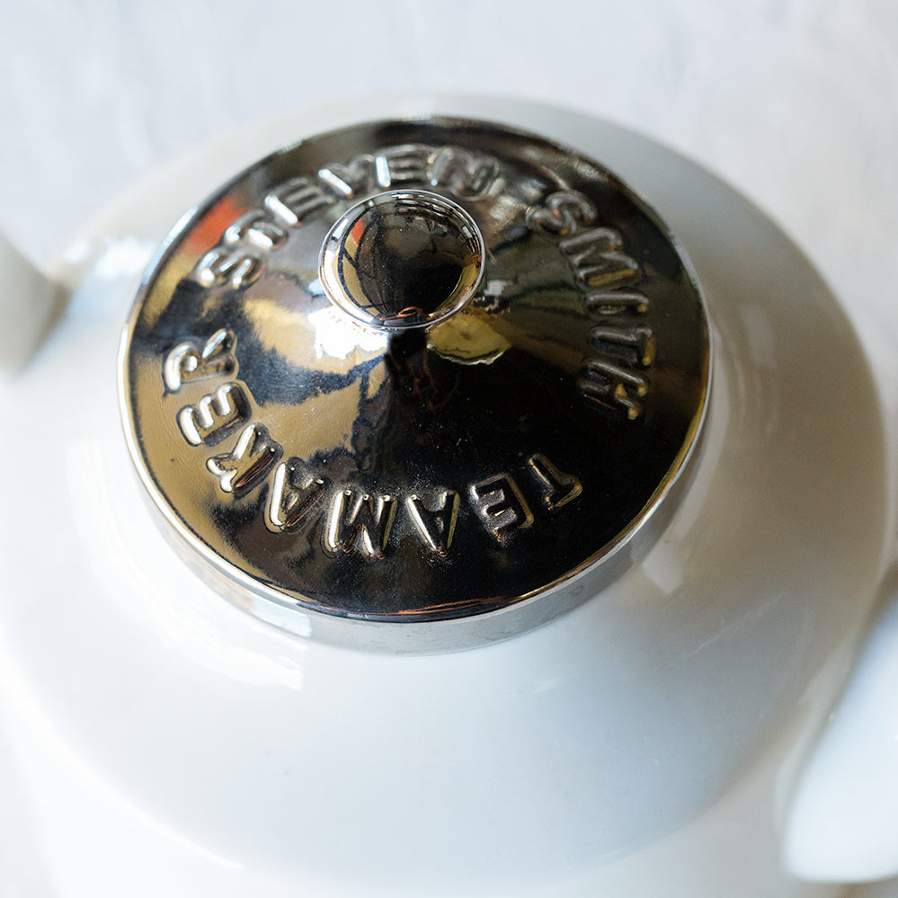 Porcelain teapot with Black smith logo and silver lid.