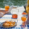 Two people sitting on the ground outside holding glasses of iced tea next to plate of pastries and pitcher of brown iced tea.